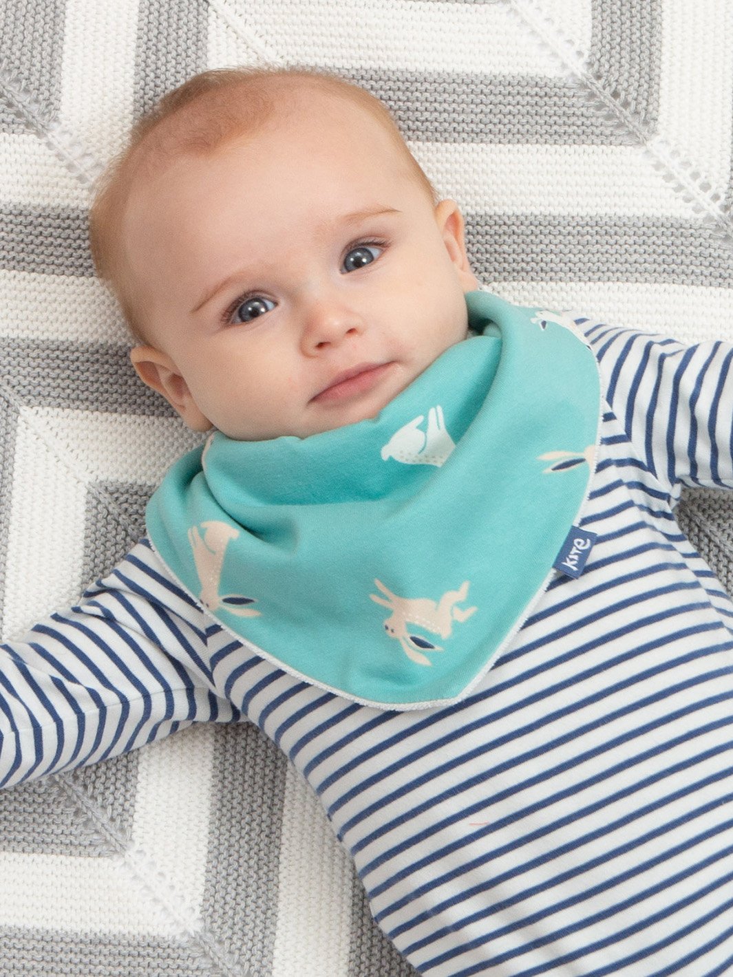 Bebé usando babero en tono aqua con estampado de conejitos, ideal para la hora de la comida, con tela suave y broche ajustable para un ajuste seguro.