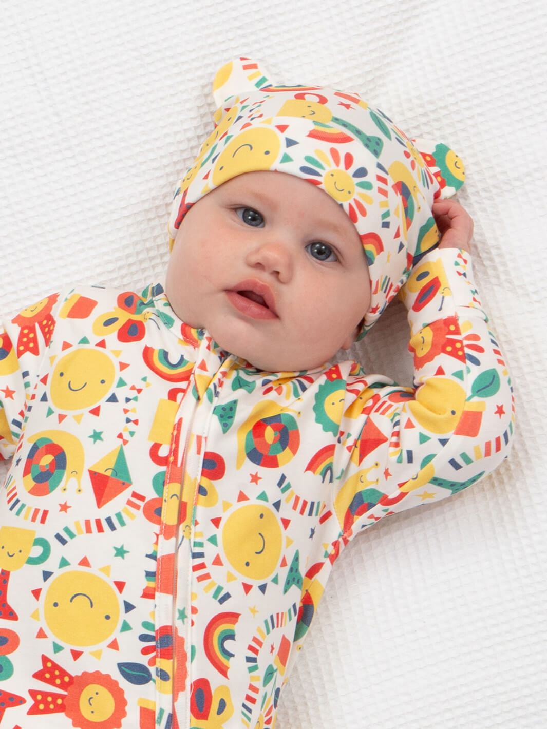 Bebé usando gorrito con orejitas, estampado de soles y arcoíris en colores vivos, de algodón orgánico.