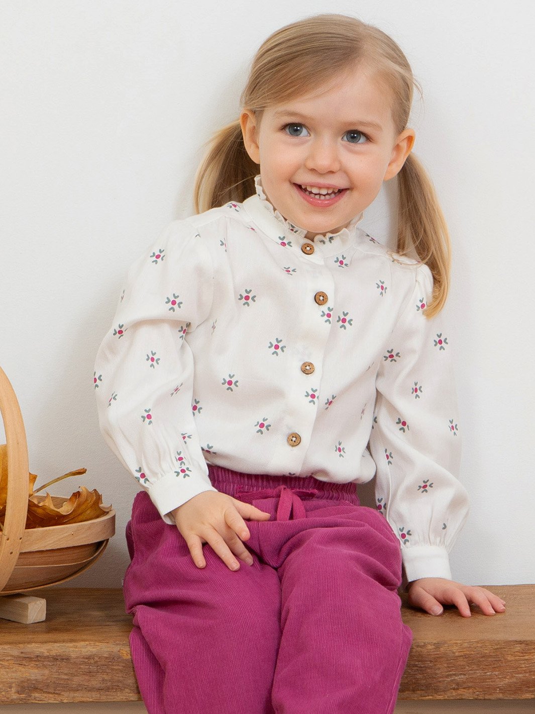 Niña vistiendo la blusa "Abrazo de amor" en algodón orgánico con cuello de volantes y puños abotonados, combinada con pantalones de cotelé rosa berry.