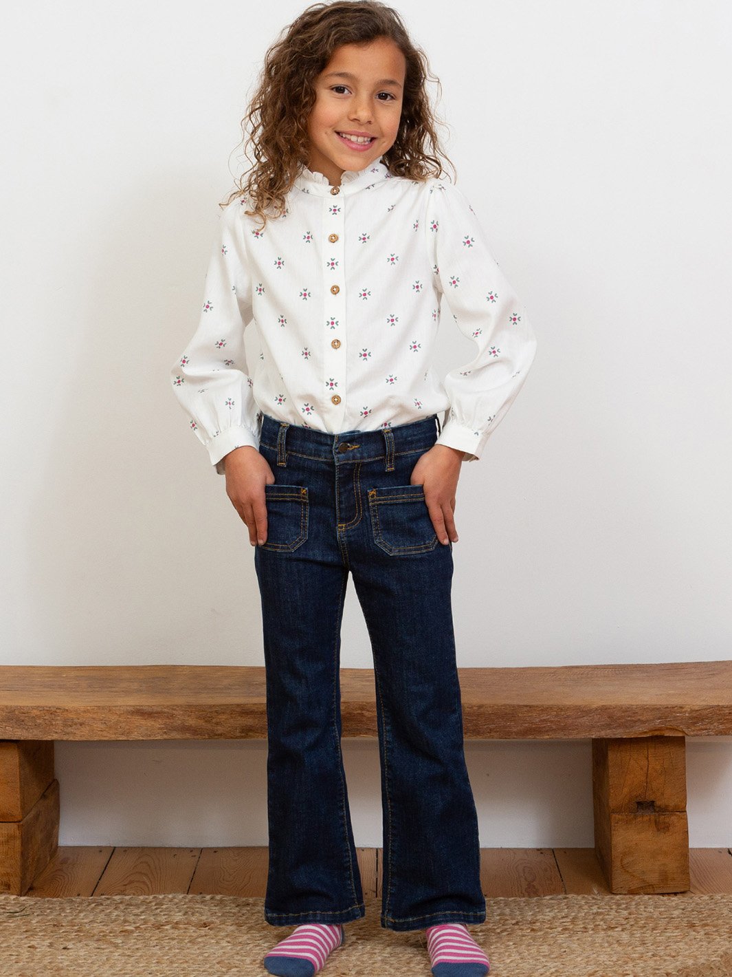 Niña vistiendo la blusa "Abrazo de amor" en algodón orgánico con cuello de volantes y puños abotonados, combinada con jeans.