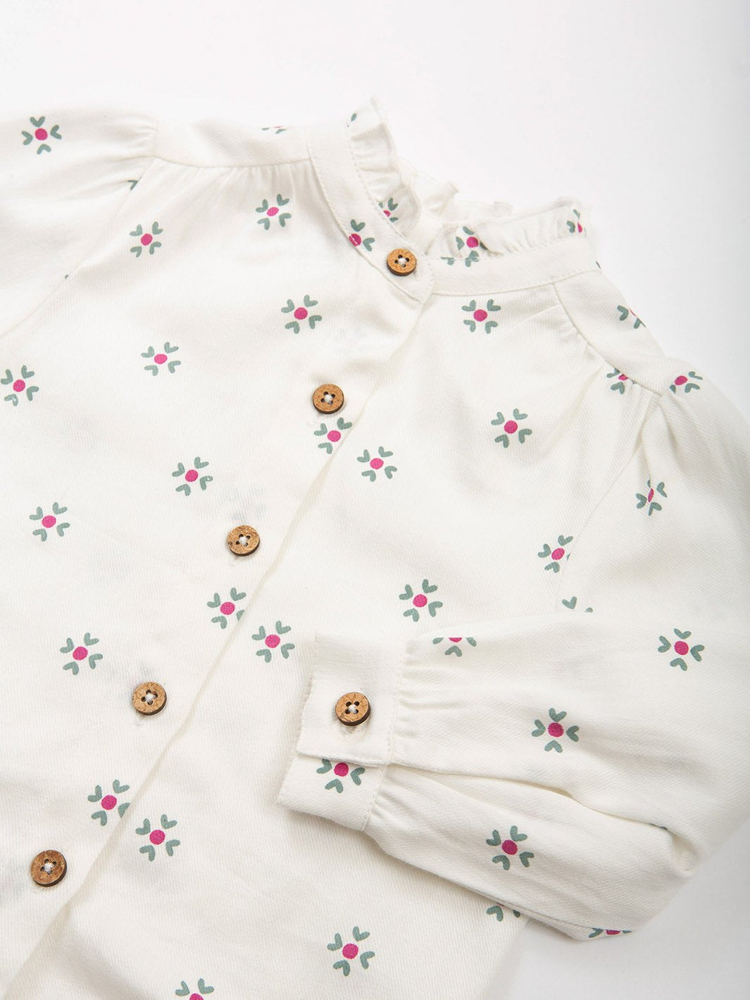 Primer plano del cuello con volantes y botones de coco de la blusa, mostrando su textura suave y delicado estampado.