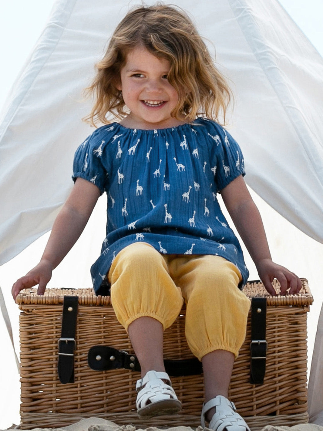 Niña vistiendo la Blusa Lunares de Jirafitas de algodón orgánico, combinada con pantalón amarillo para un look fresco y versátil.