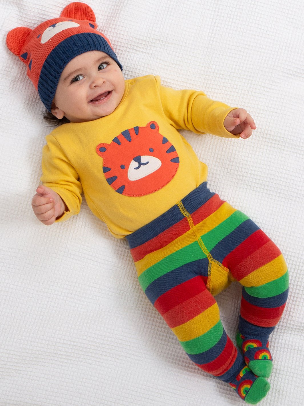 Bebé vistiendo el body de manga larga Tigre Top en amarillo maíz, combinado con calzas tejidas y un gorro a juego, creando un conjunto acogedor y adorable en algodón orgánico.