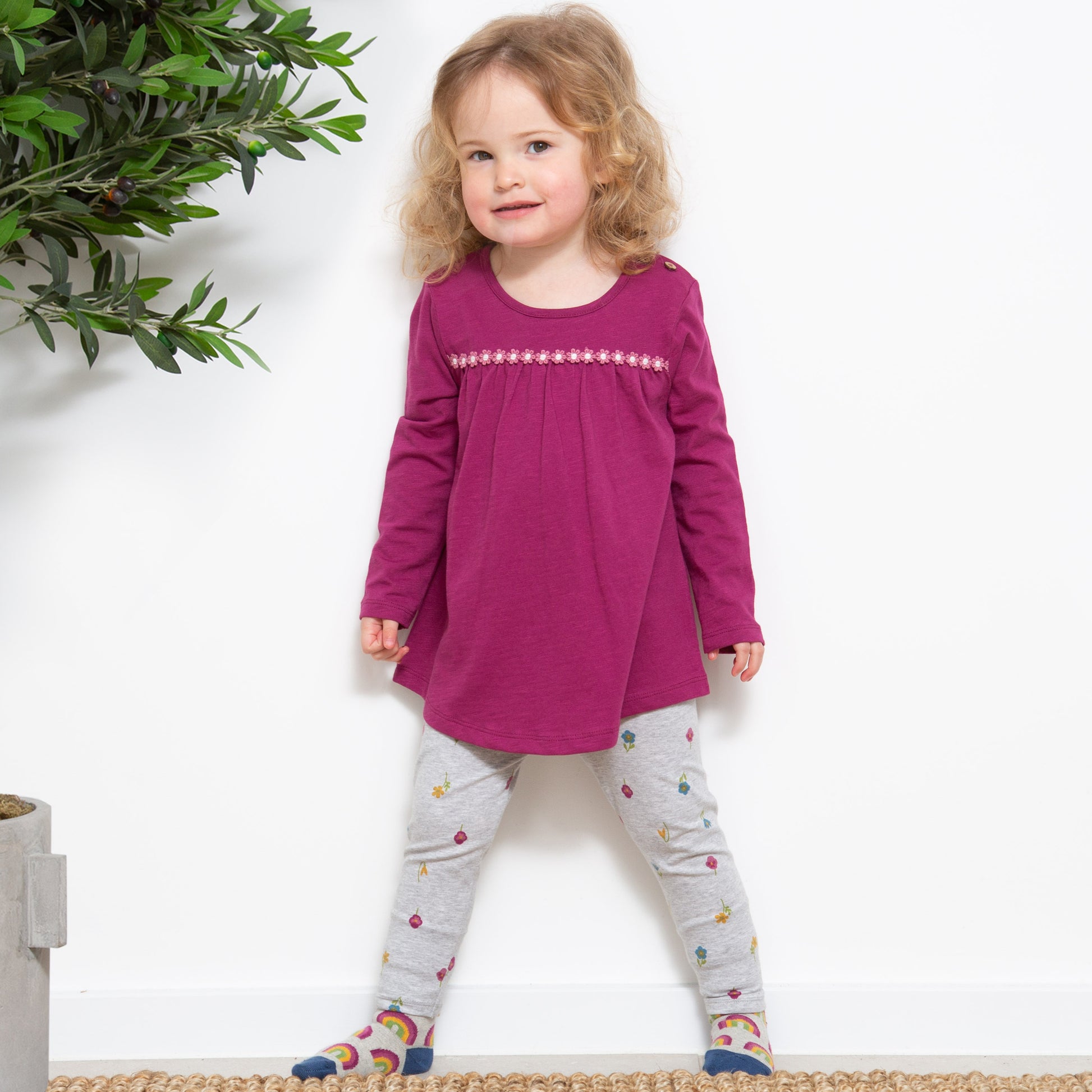 Niña vistiendo las Calzas Print de algodón orgánico con estampado de pequeñas flores sobre fondo gris, look elegante y cómodo para cualquier ocasión.