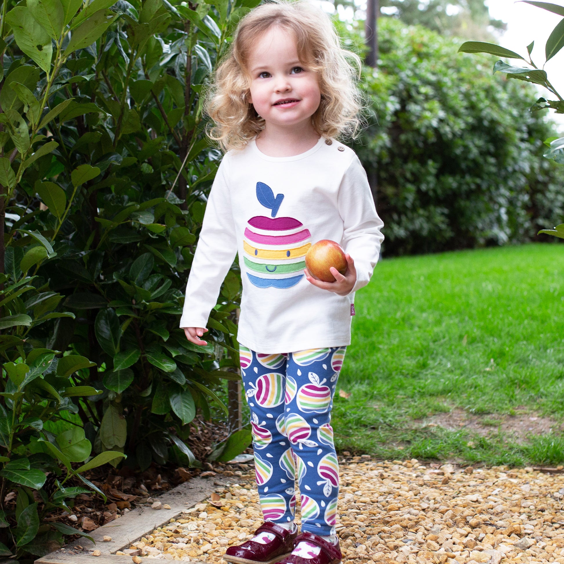 Niña vistiendo las Calzas Print de algodón orgánico con estampado de manzanas arcoíris, look cómodo y encantador para el día a día.
