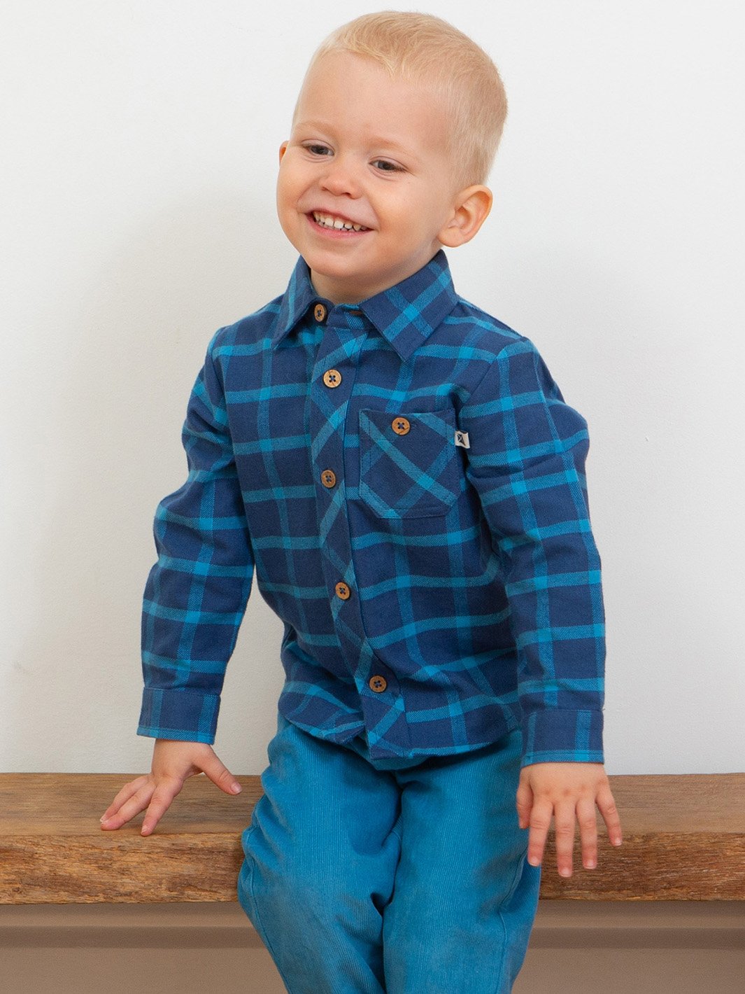 Niño vistiendo camisa de franela a cuadros azul marino y calipso, combinada con pantalones de cotelé para un look moderno y versátil.