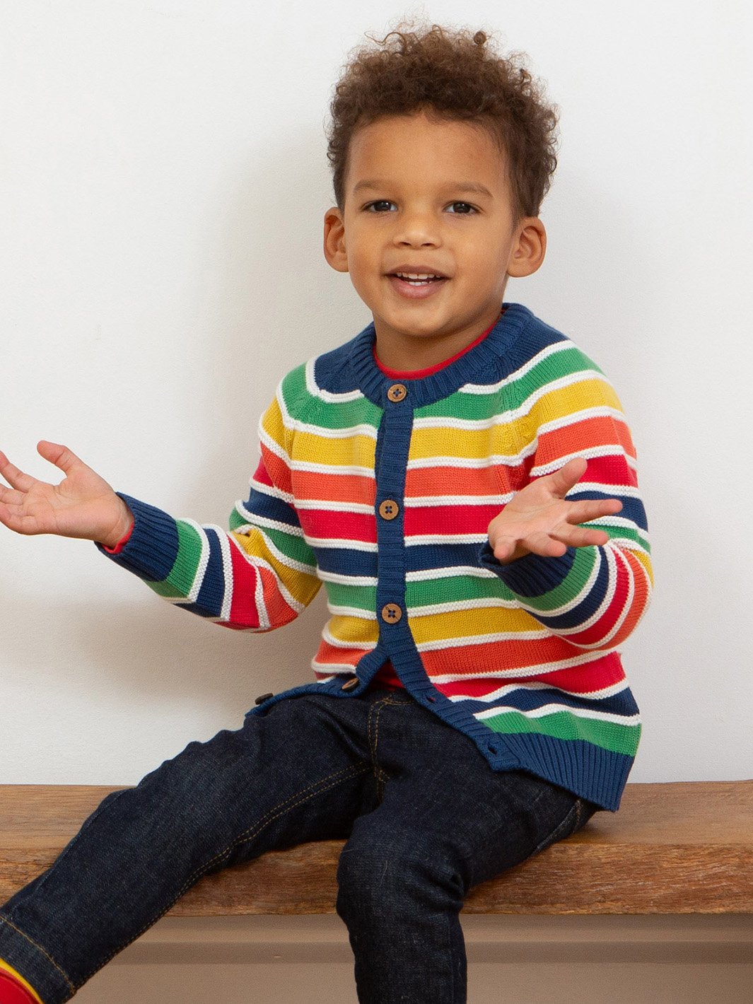 Niño usando el chaleco tejido arcoíris, destacando su ajuste cómodo, tejido de punto suave y vibrante combinación de colores.