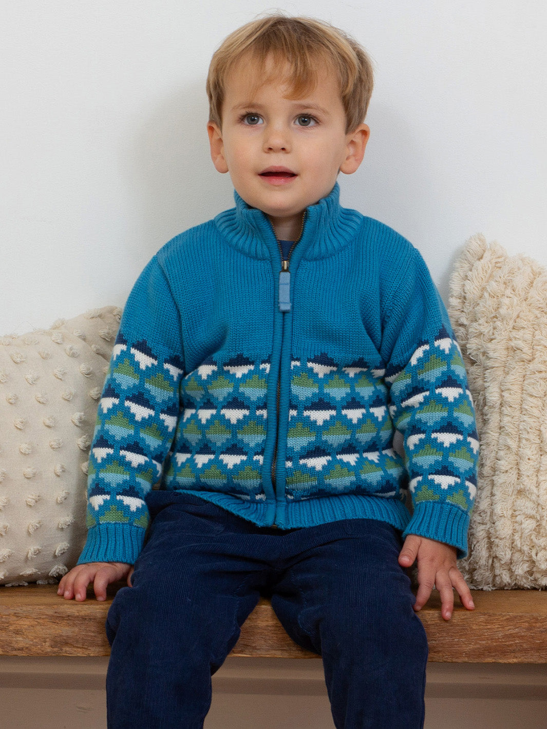 Niño usando chaqueta Nido azul clásico de algodón orgánico con diseño geométrico de triángulos verdes y blancos, abrigo de invierno infantil.