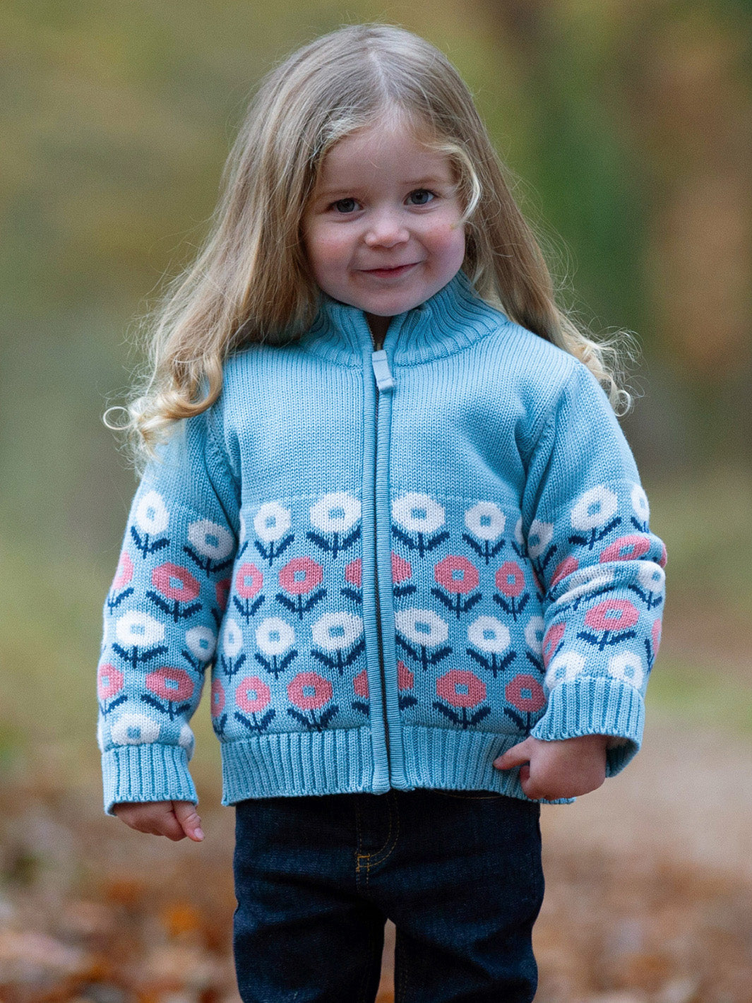 Niña usando chaqueta Nido celeste de algodón orgánico con diseño de flores rosas y blancas, ideal como abrigo de invierno para bebé y niño.