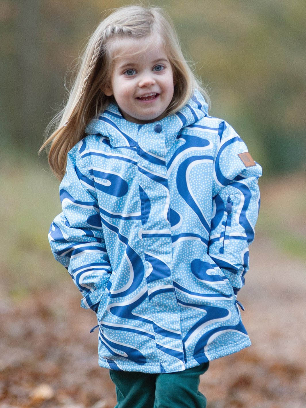 Niña vistiendo la chaqueta impermeable Nimbus con estampado Snow Run en azul iceberg, con manos en los bolsillos, mostrando su ajuste cómodo y diseño resistente al frío y la nieve.