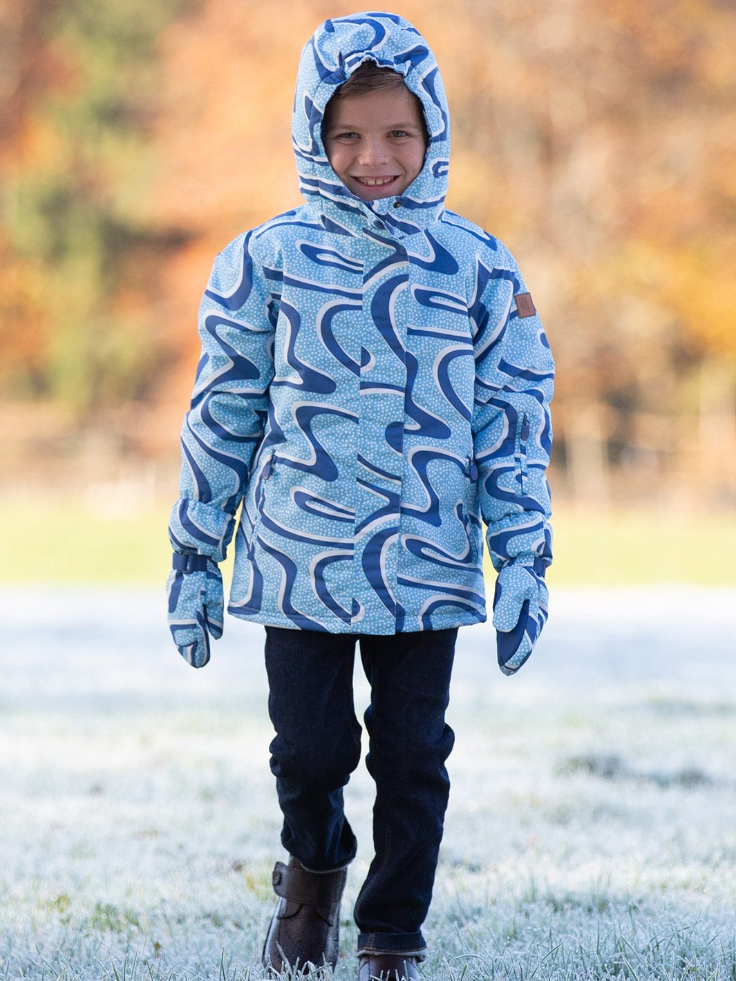 Niño vistiendo chaqueta impermeable azul iceberg con forro térmico y falda de nieve, disfrutando de un día de aventura invernal. La capucha y el diseño resistente al agua lo protegen del frío y la lluvia.