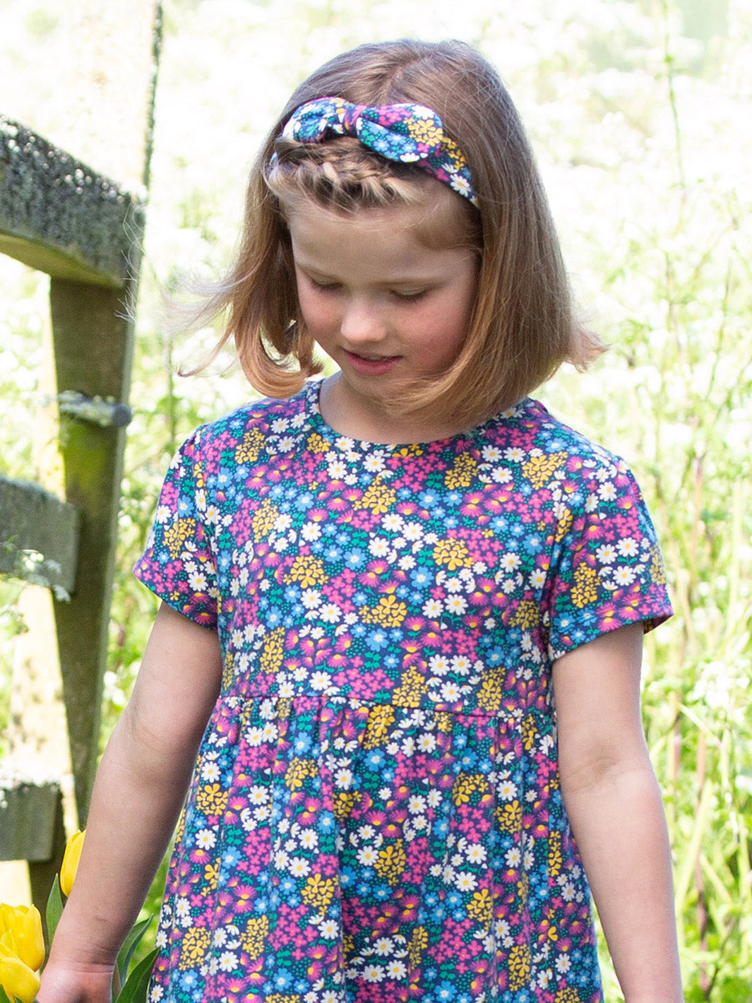 Niña con cintillo de algodón orgánico con estampado de jardín de flores y lazo decorativo, combinando con un vestido a juego.