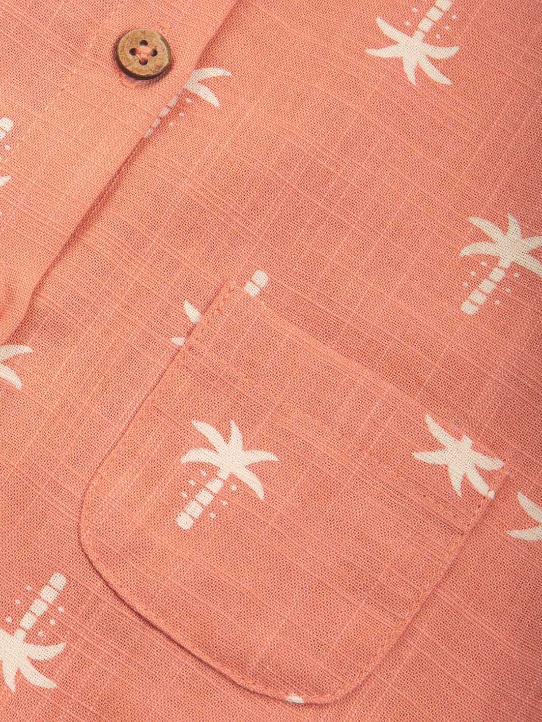 Detalle del bolsillo y botones de madera en enterito sin mangas color coral con estampado de palmeras.