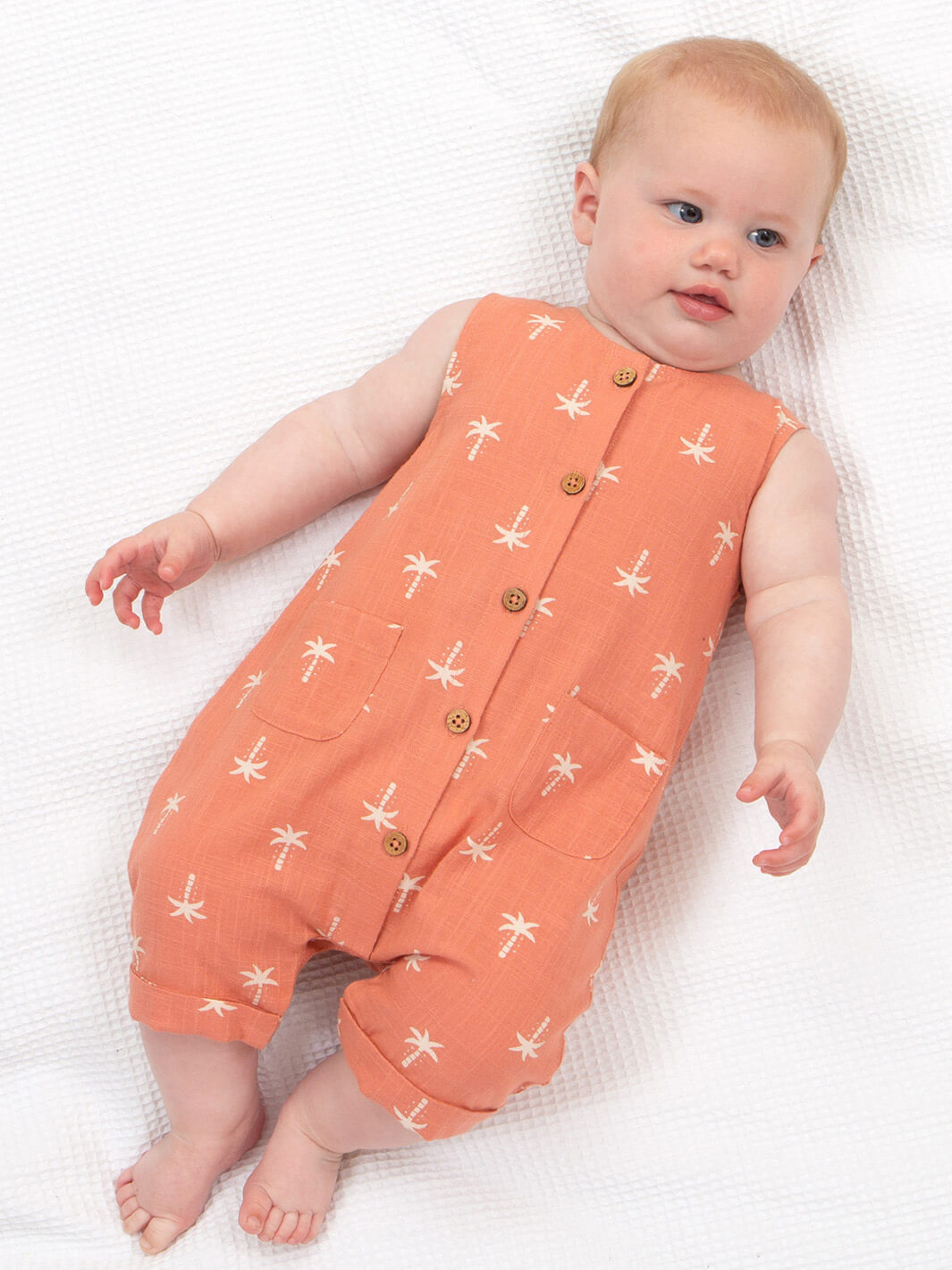 Bebé usando enterito sin mangas coral con palmeras blancas, ropa cómoda y fresca para verano.