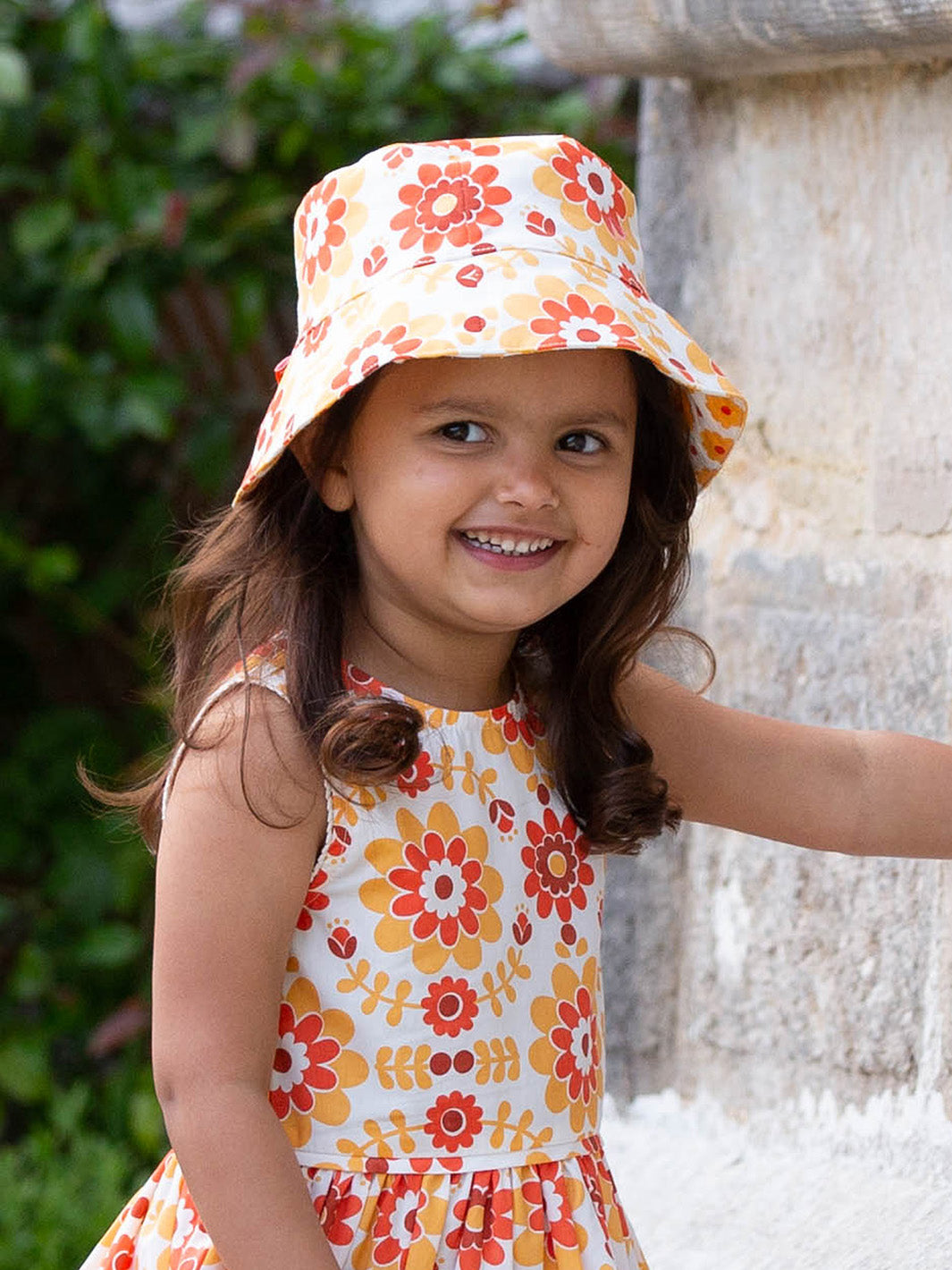 Niña disfrutando al aire libre con el sombrero de algodón orgánico amarillo con estampado de flores retro y borde protector.
