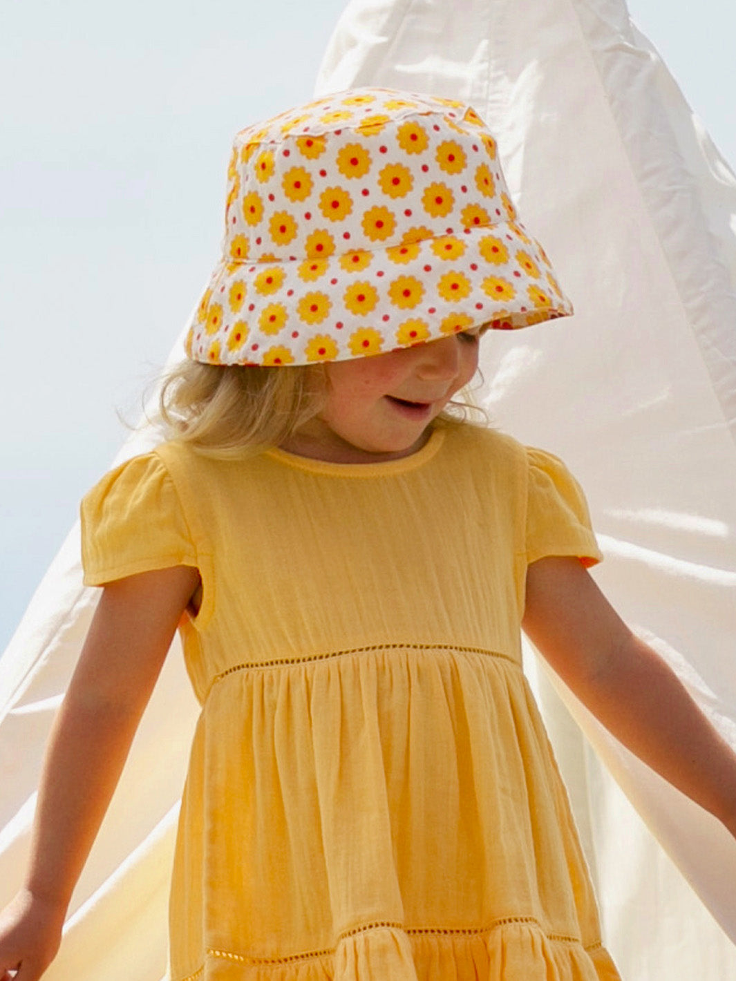Niña con sombrero de algodón amarillo con estampado de lunares, ideal para el verano y la protección solar.