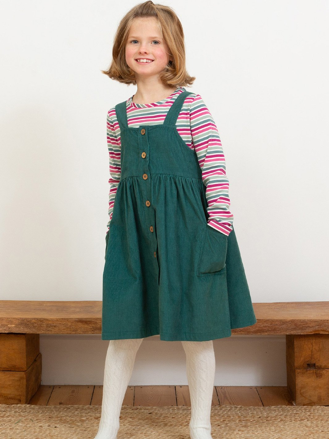 Niña de 6 años vistiendo jardinera de algodón orgánico verde pino, combinada con una polera, logrando un look cómodo.