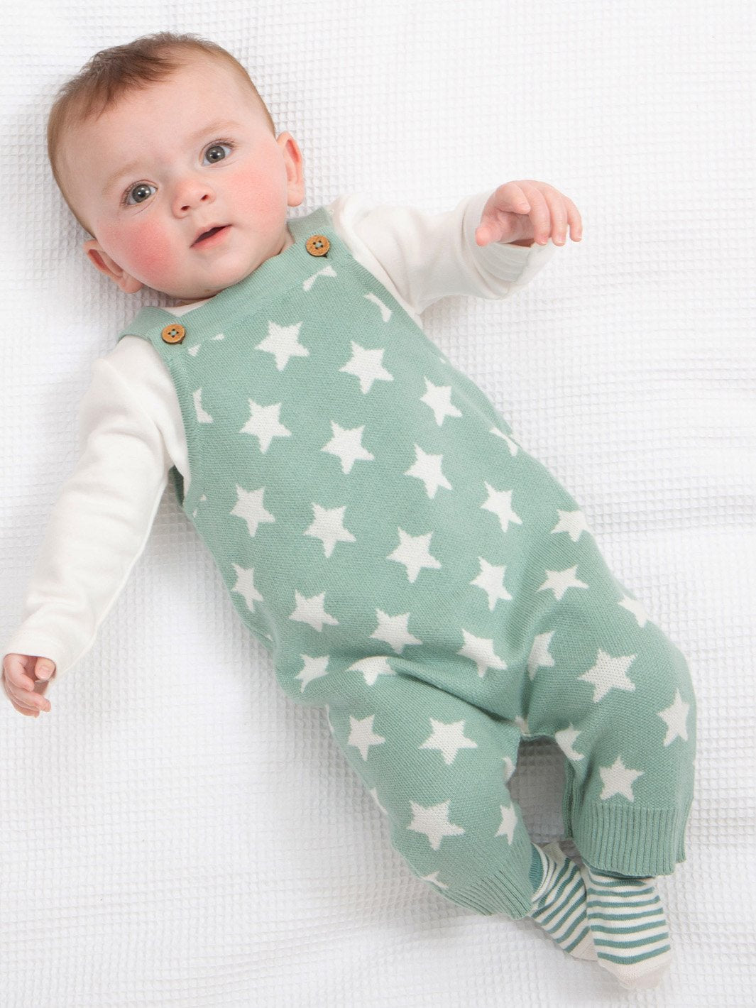Bebé cómodo con la jardinera tejida con estrellas en color verde abeto, en combinación con body blanco y calcetines a juego.