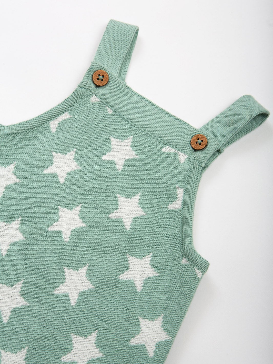 Primer plano de la jardinera tejida con estrellas, mostrando la textura del tejido ojo de ave, los botones de coco en los tirantes y el patrón de estrellas en jacquard.