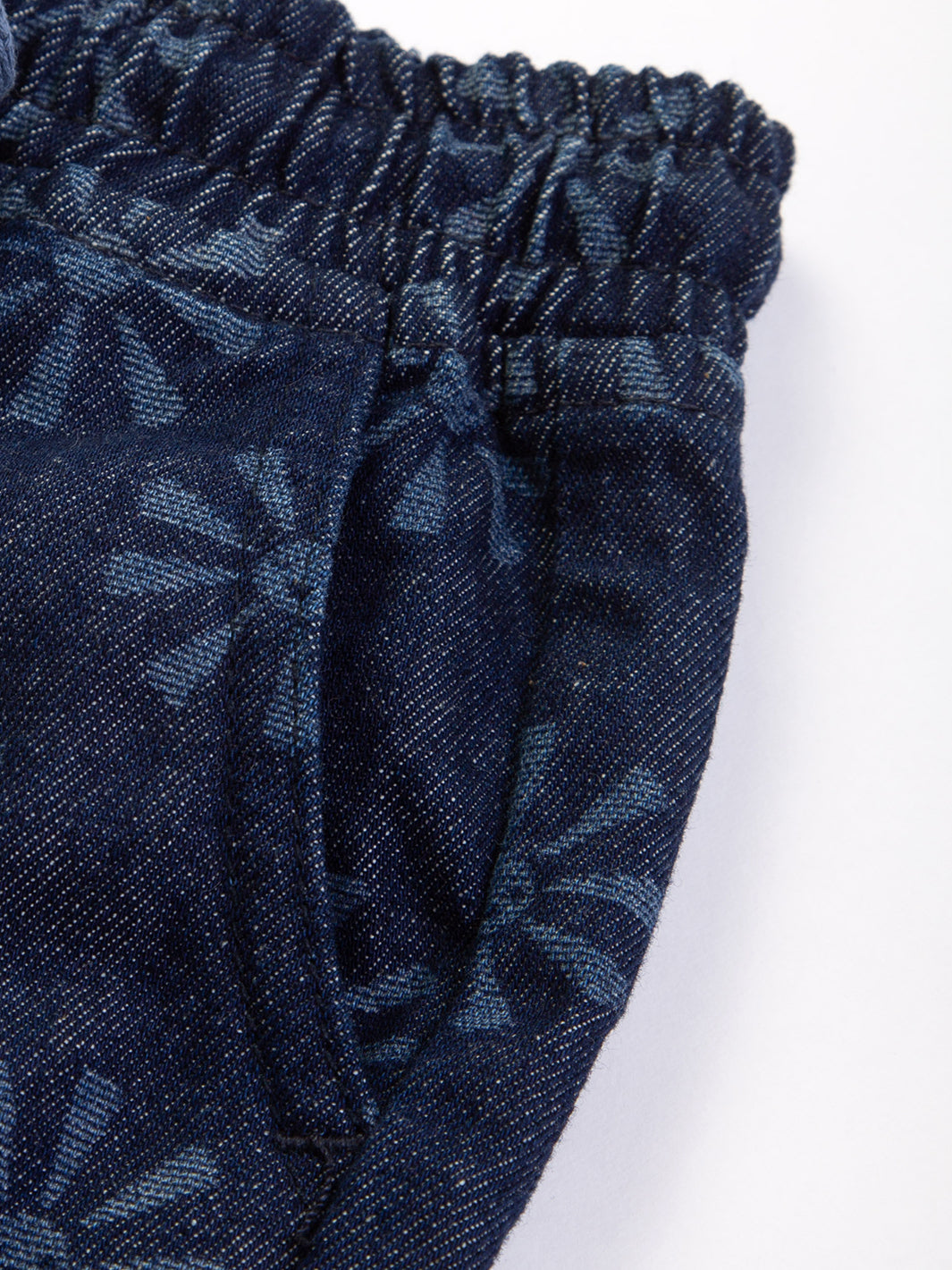 Primer plano del estampado de soles sonrientes en jeans de algodón orgánico, resaltando el diseño grabado en láser, cinturilla elástica y la textura de la mezclilla liviana.