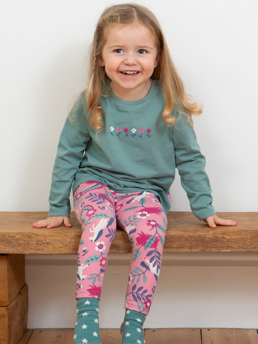 Bebé usando leggings rosa bebé de algodón orgánico con estampado de ponys y cerditos, combinados con una polerón para un look dulce y cómodo.