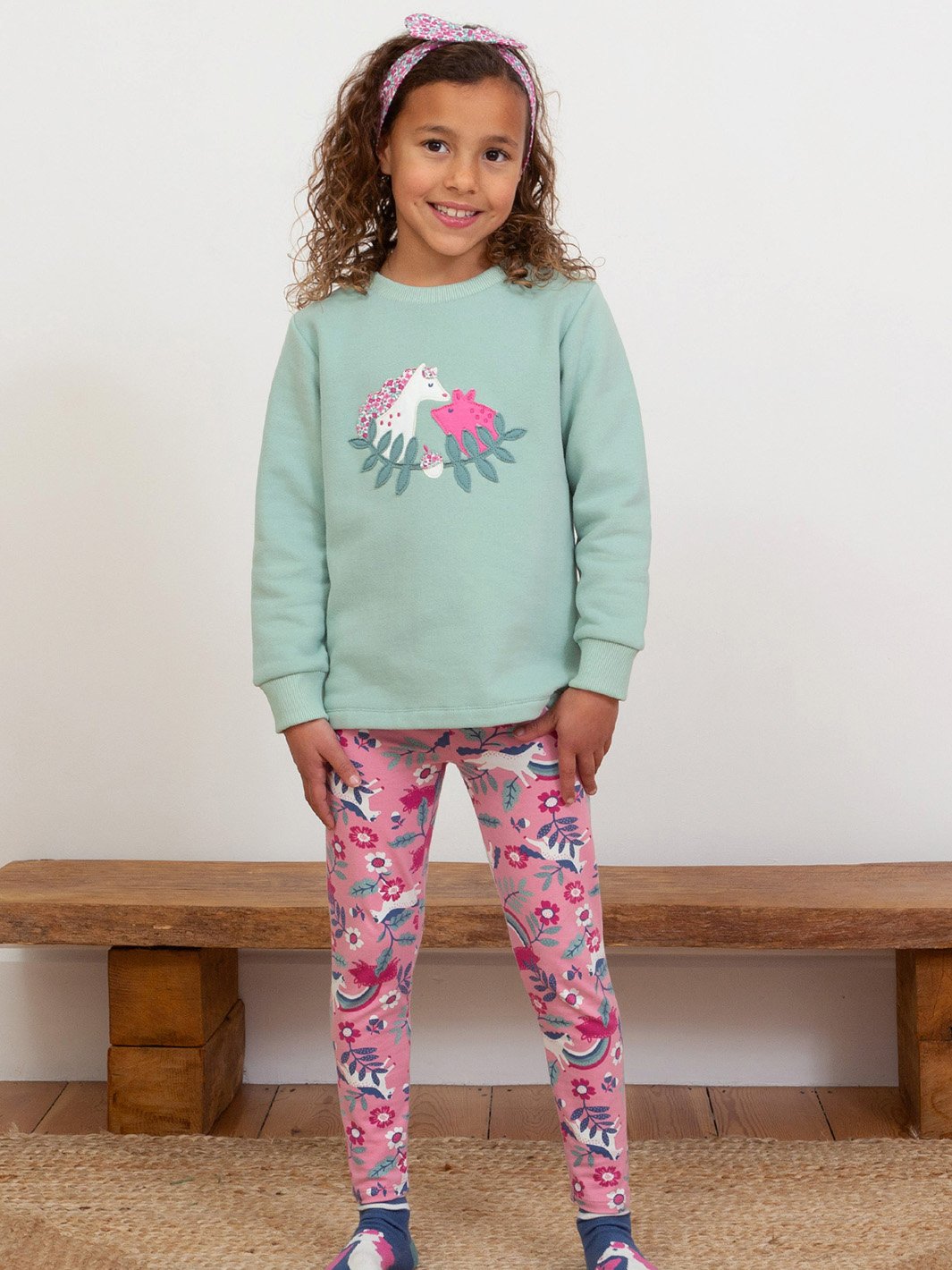 Niña usando leggings rosa de algodón orgánico con estampado de ponys y cerditos, combinados con un polerón a juego, para un look dulce y cómodo.
