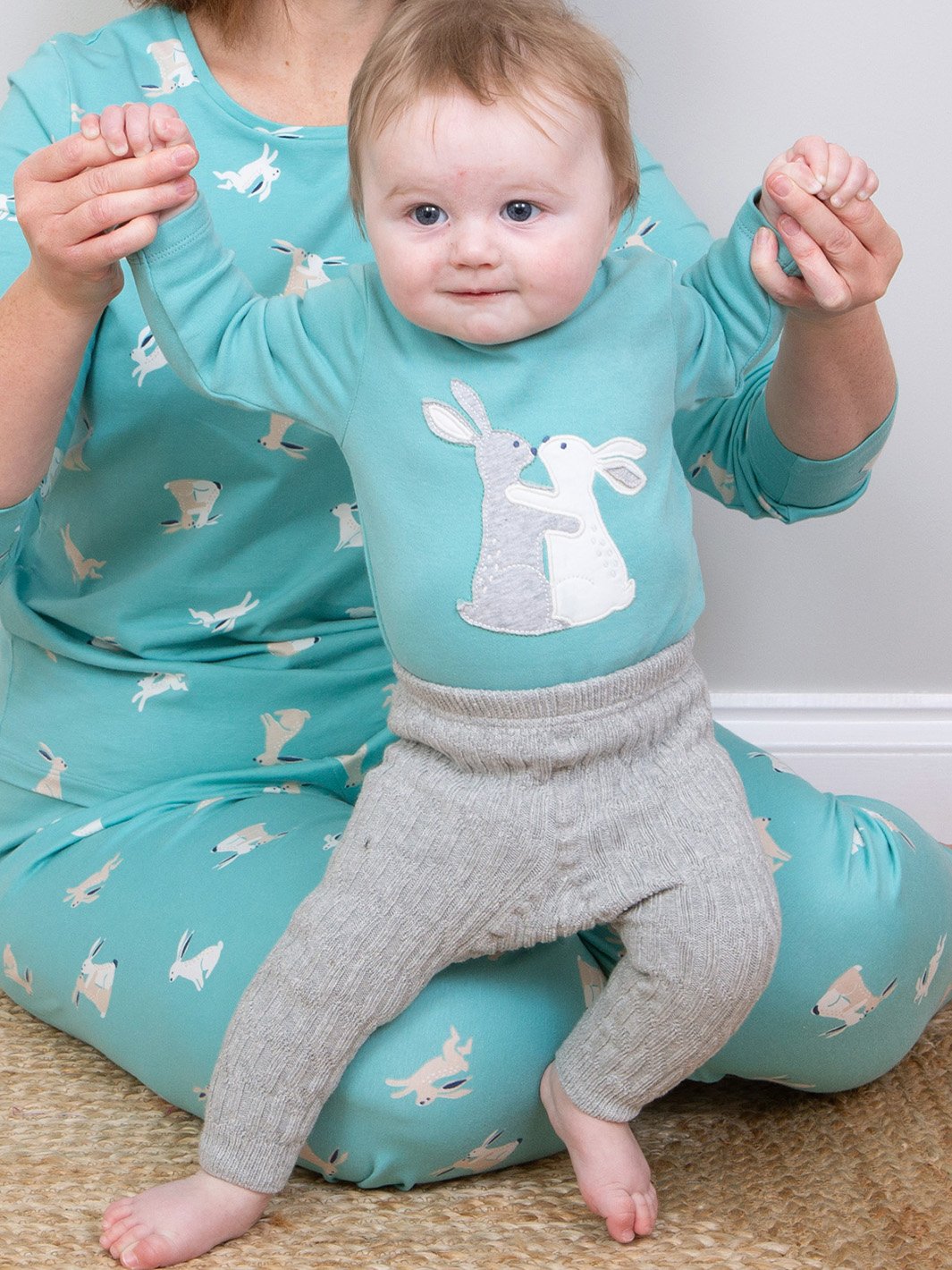 Bebé vistiendo el body Abrazo de Conejito, combinado con leggings tejidos trenzados en gris jaspeado, creando un look tierno y acogedor.