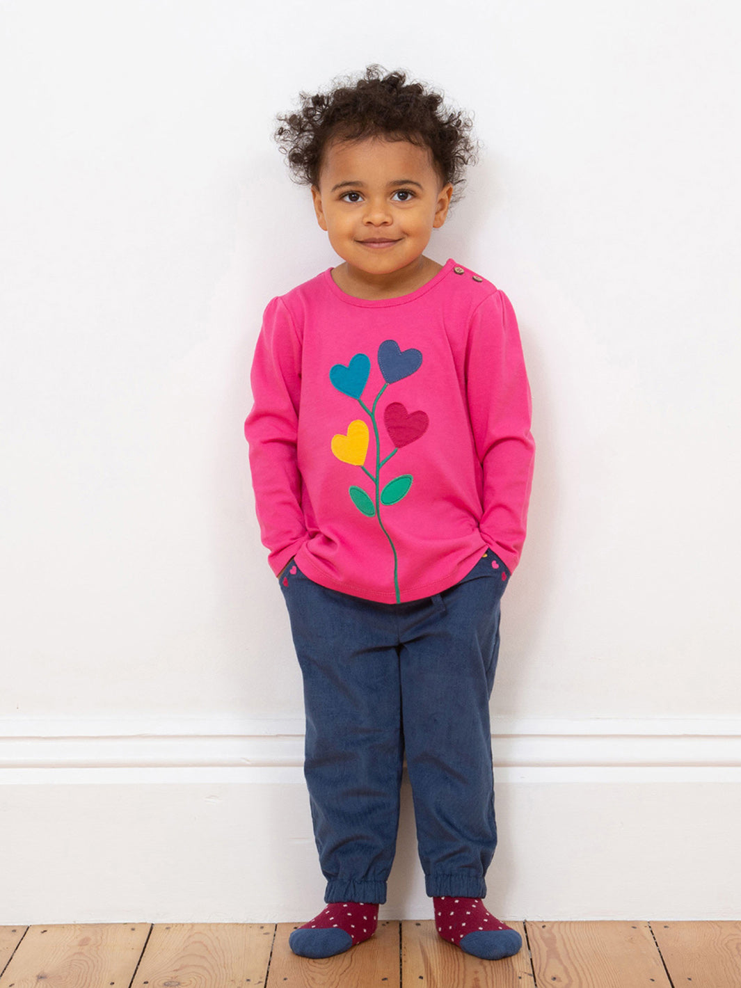Niña usando el Pantalón Cotelé Corazones de algodón orgánico, combinado con un suéter para un look moderno y acogedor.