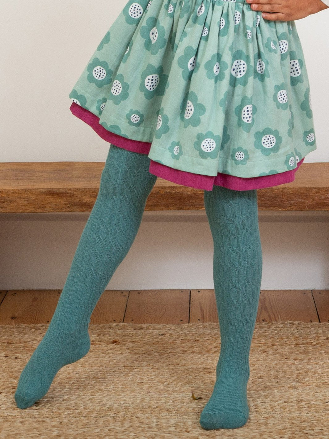 Niña vistiendo las pantys de algodón orgánico verde abeto, resaltando su diseño de punto trenzado, en combinación con una falda.
