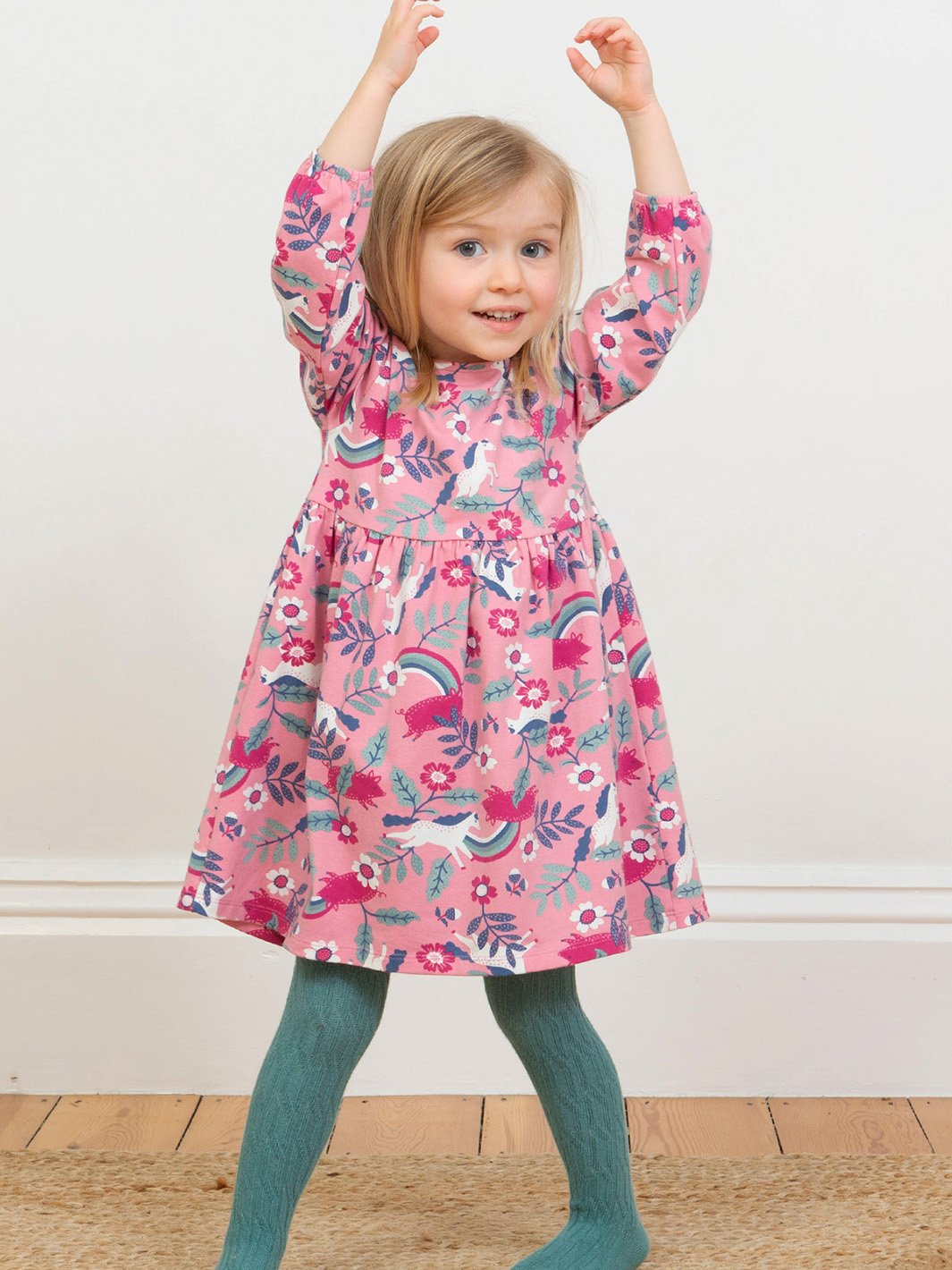 Niña usando pantys de algodón orgánico en color verde abeto con diseño de punto trenzado, combinadas con un vestido, para un look cómodo y acogedor.