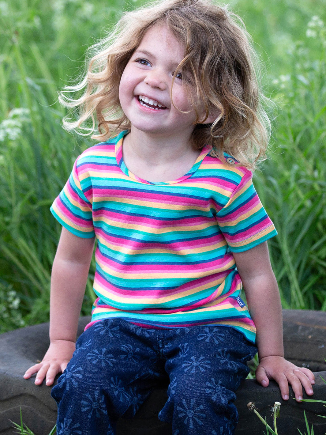Niña usando la Polera Arcoíris de algodón orgánico, combinada con un short para un look fresco y alegre.