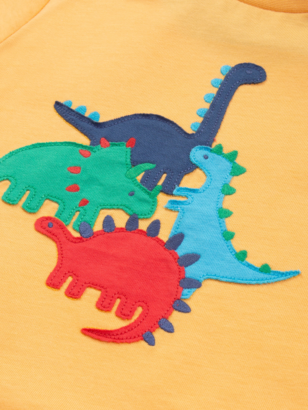 Detalle del aplique de dinosaurio en la Polera Juego de Dinosaurios de algodón orgánico, diseño divertido y certificado OEKO-TEX.