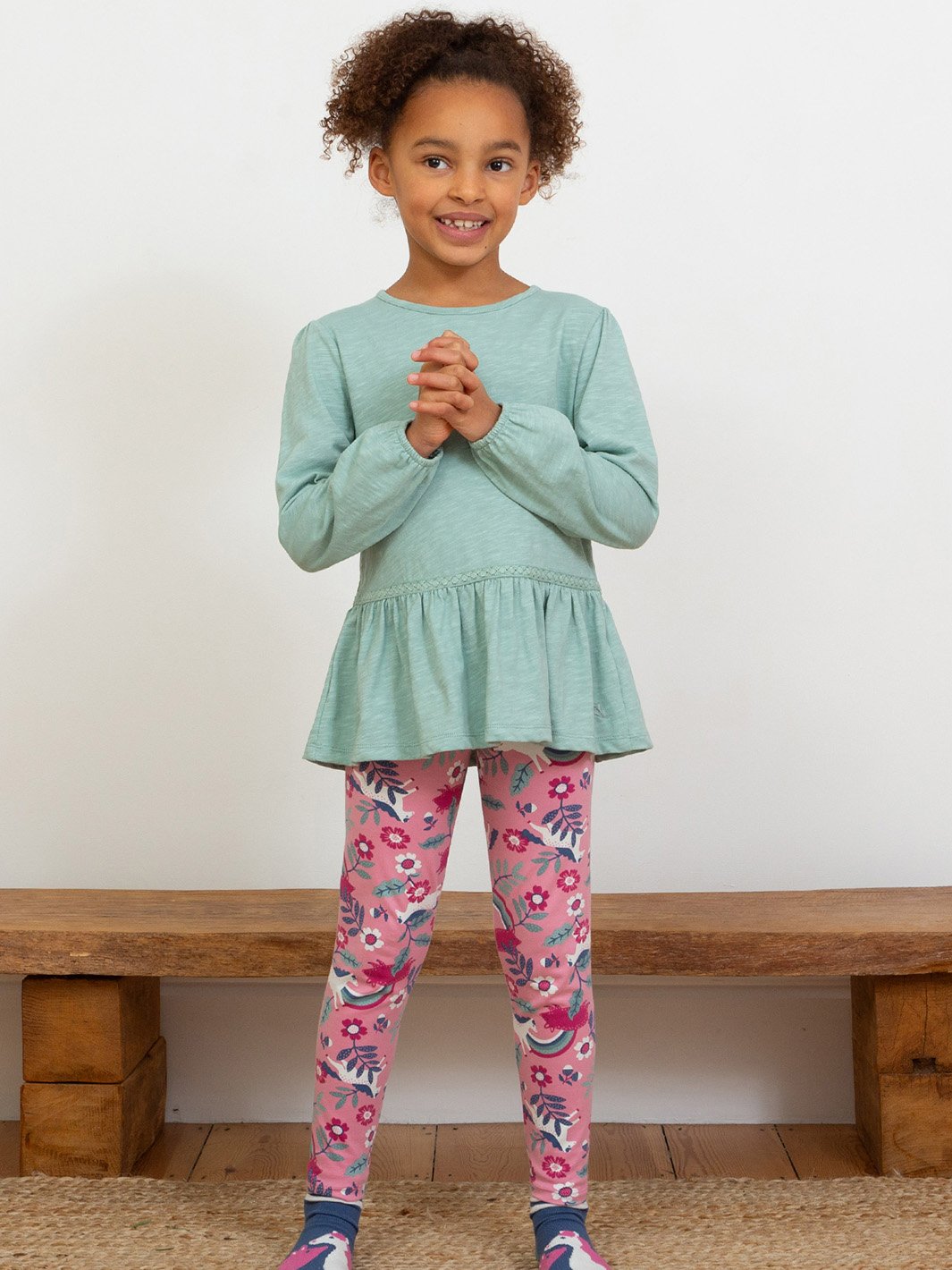 Niña usando la polera túnica verde abeto suave, combinada con calzas, mostrando su estilo holgado y detalles femeninos.