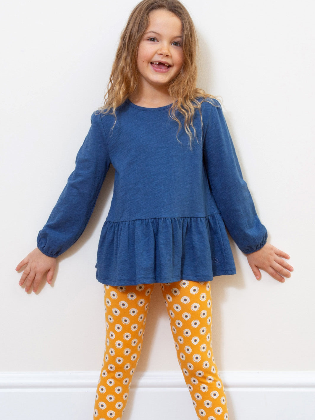 Niña luciendo la polera azul marino con volantes, combinada con calzas de algodón orgánico, perfecta para bailar y girar con estilo.