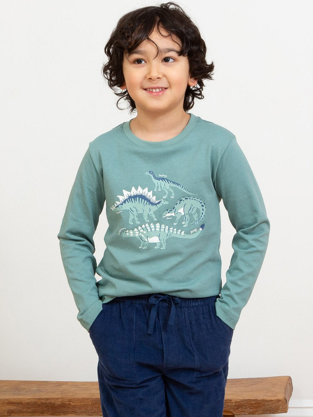 Niño con polera de manga larga verde abeto, mostrando el estampado de dinosaurios en combinación con pantalones de cotelé para un look cómodo y abrigado.