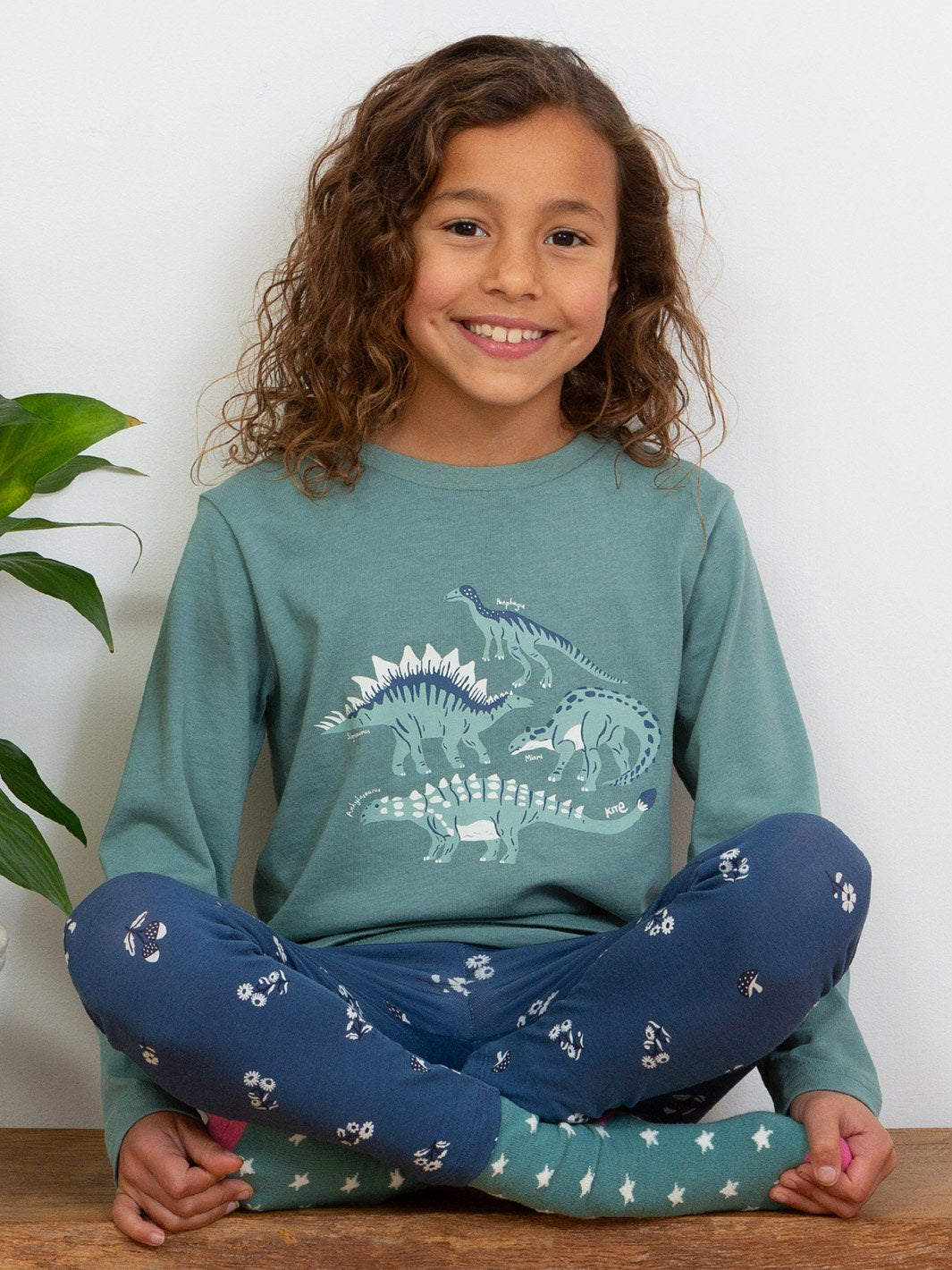 Niña con polera de manga larga verde abeto, mostrando el estampado de dinosaurios en un look cómodo y versátil.