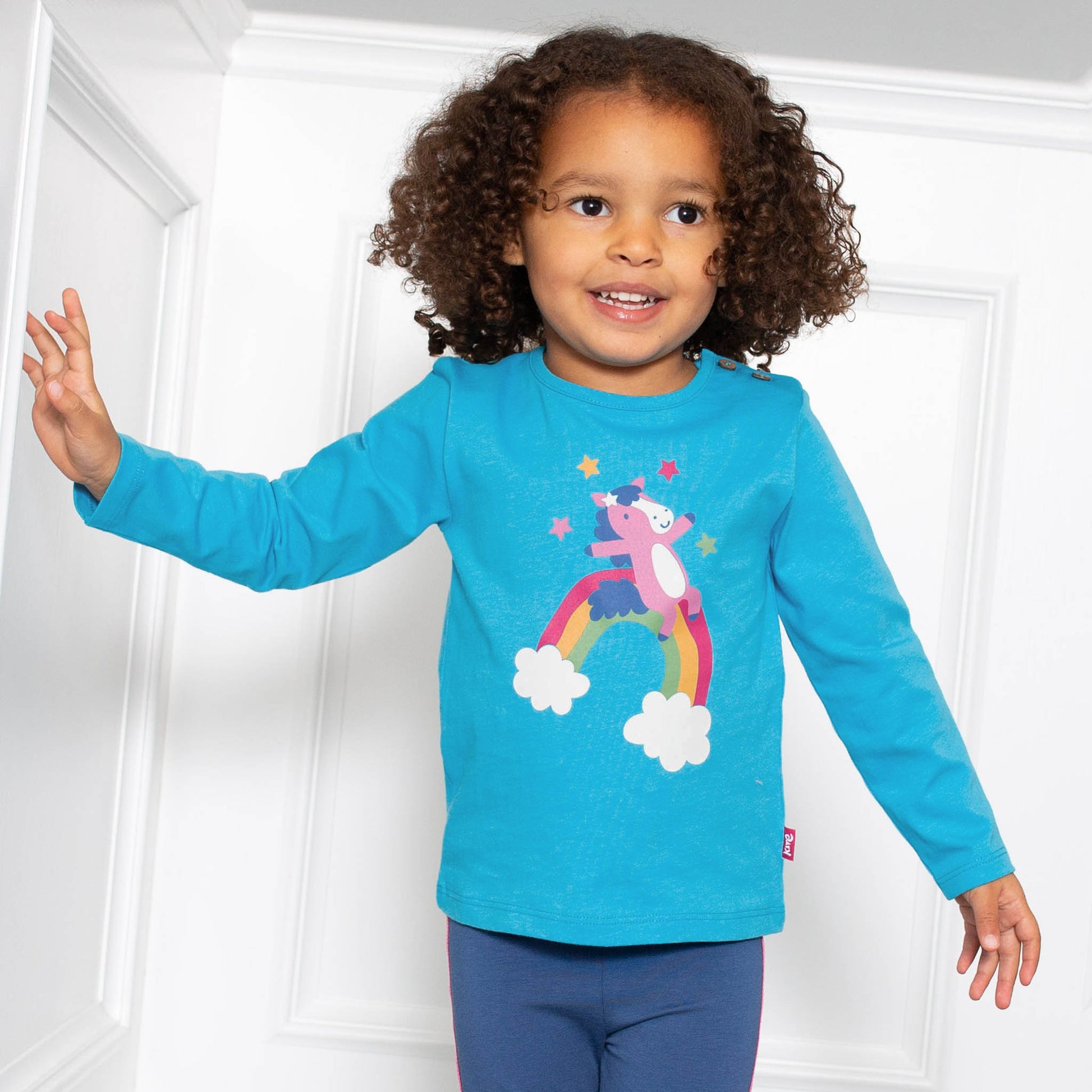 Niña vistiendo la Polera Pony Arcoíris con calzas de algodón orgánico, look ideal para días llenos de magia y color.