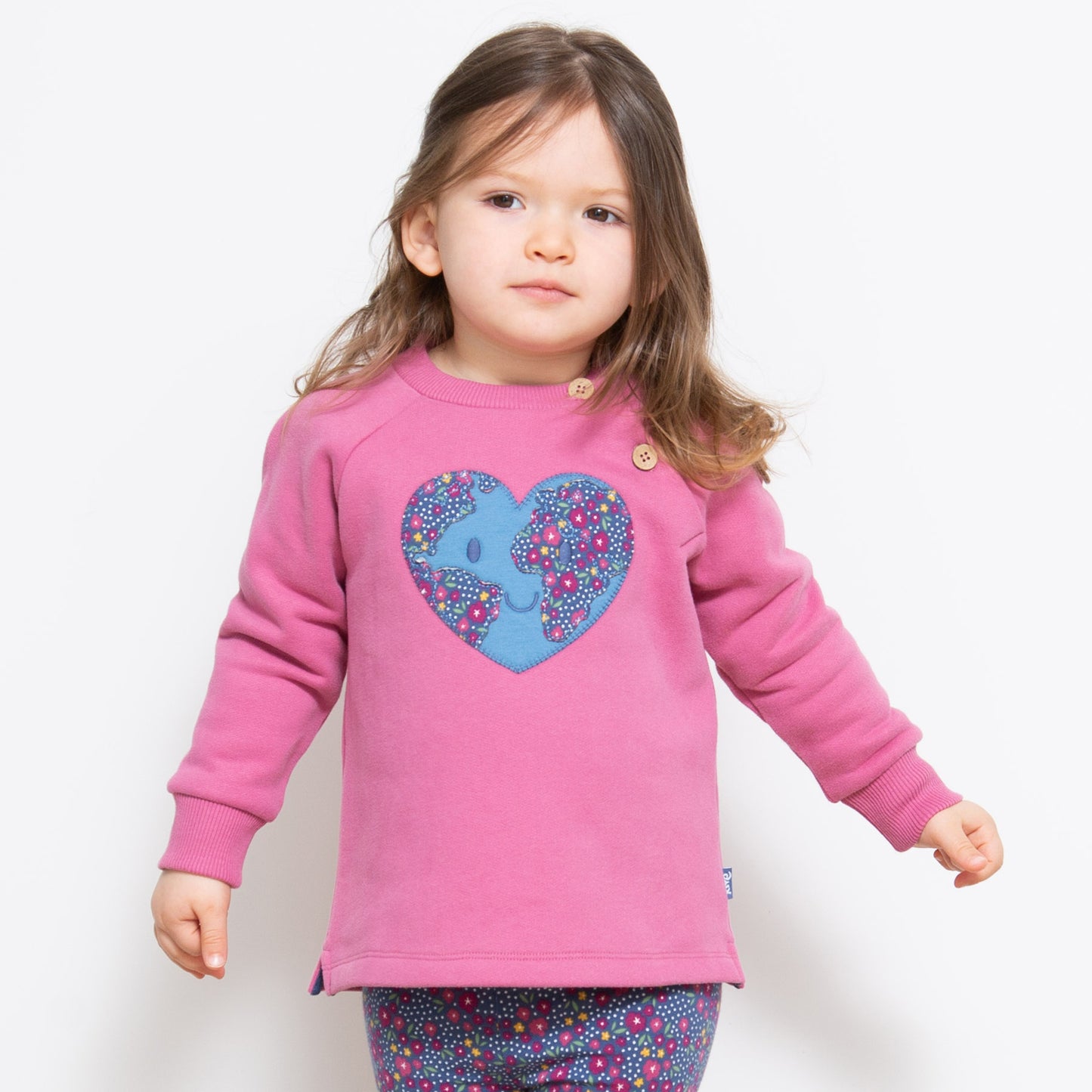 Niña usando el Polerón Planeta Amor de algodón orgánico, combinado con calzas Florcitas Caseras para un look tierno y ecológico.