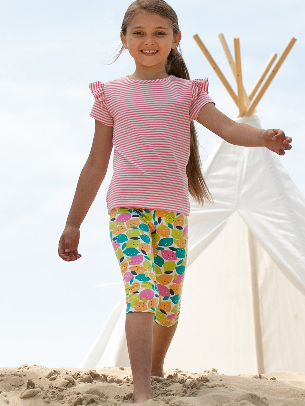 Niña vistiendo calzas 3/4, de algodón orgánico con estampado de frutas cítricas, combinadas con una polera para un look alegre y veraniego.