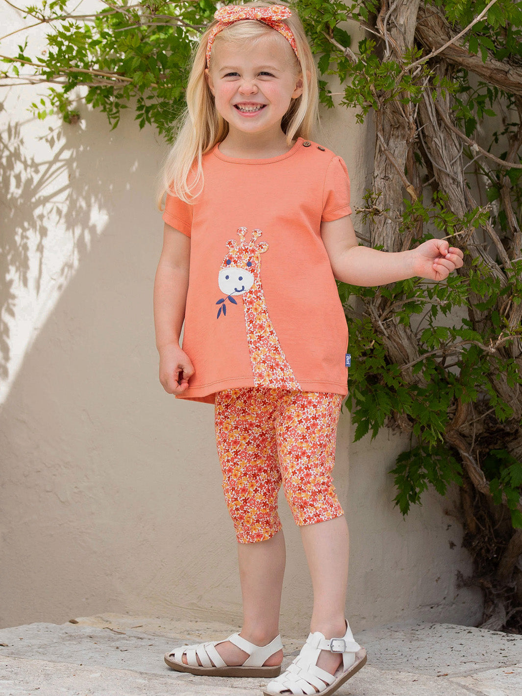 Niña vistiendo calzas 3/4 de algodón orgánico con estampado de flores naranjas, combinadas con una polera para un look fresco y alegre.