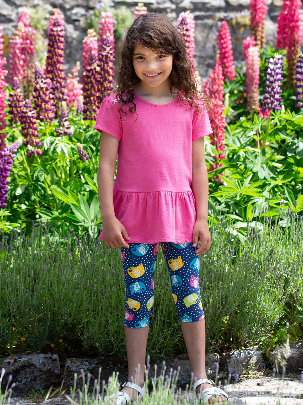 Niña vistiendo las calzas 3/4 con estampado de elefantes, combinadas con una polera rosa para un look fresco y cómodo