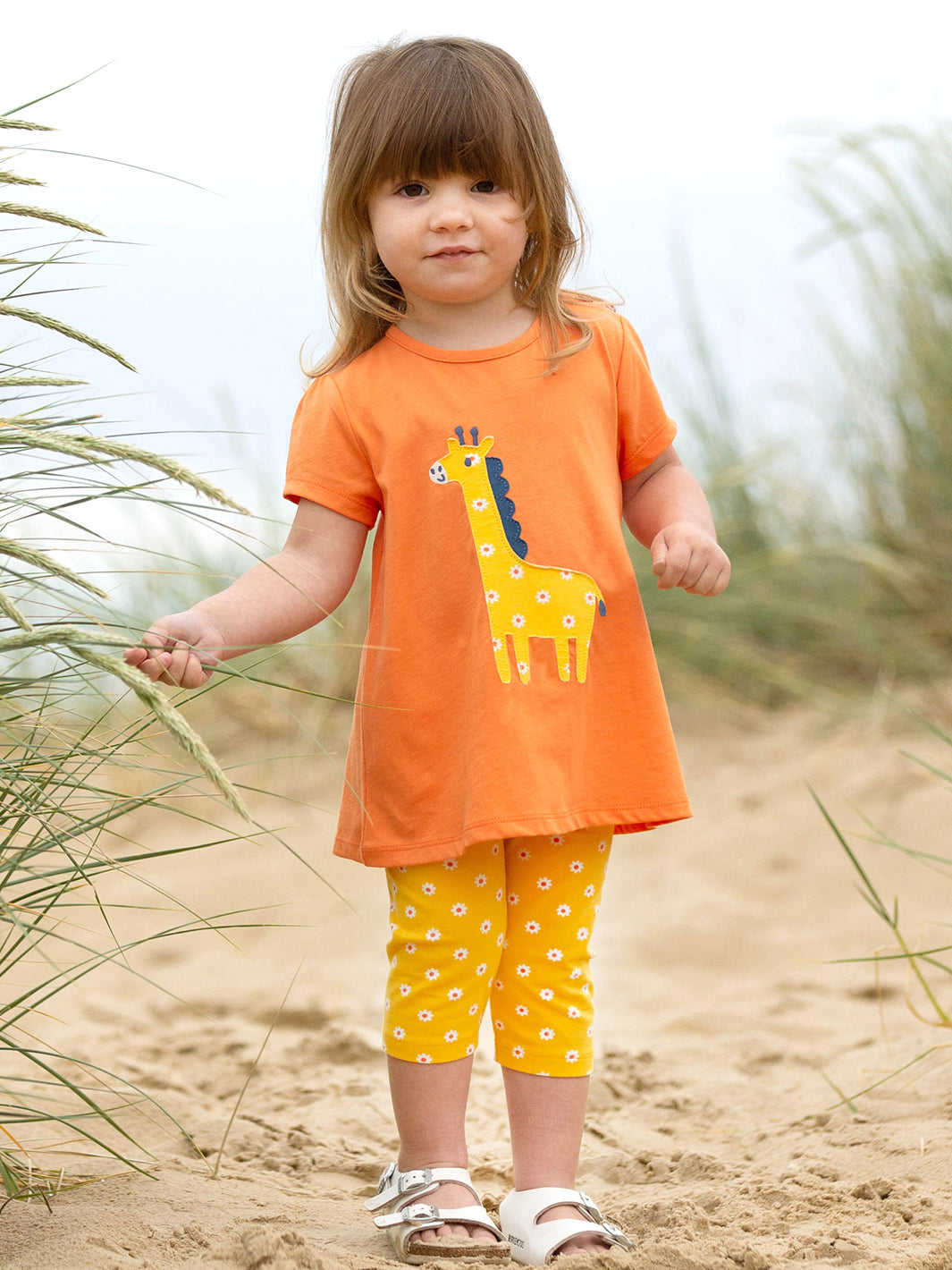 Niña vistiendo calzas 3/4 de algodón orgánico en amarillo con estampado de margaritas, combinadas con una polera a juego para un look fresco y alegre.