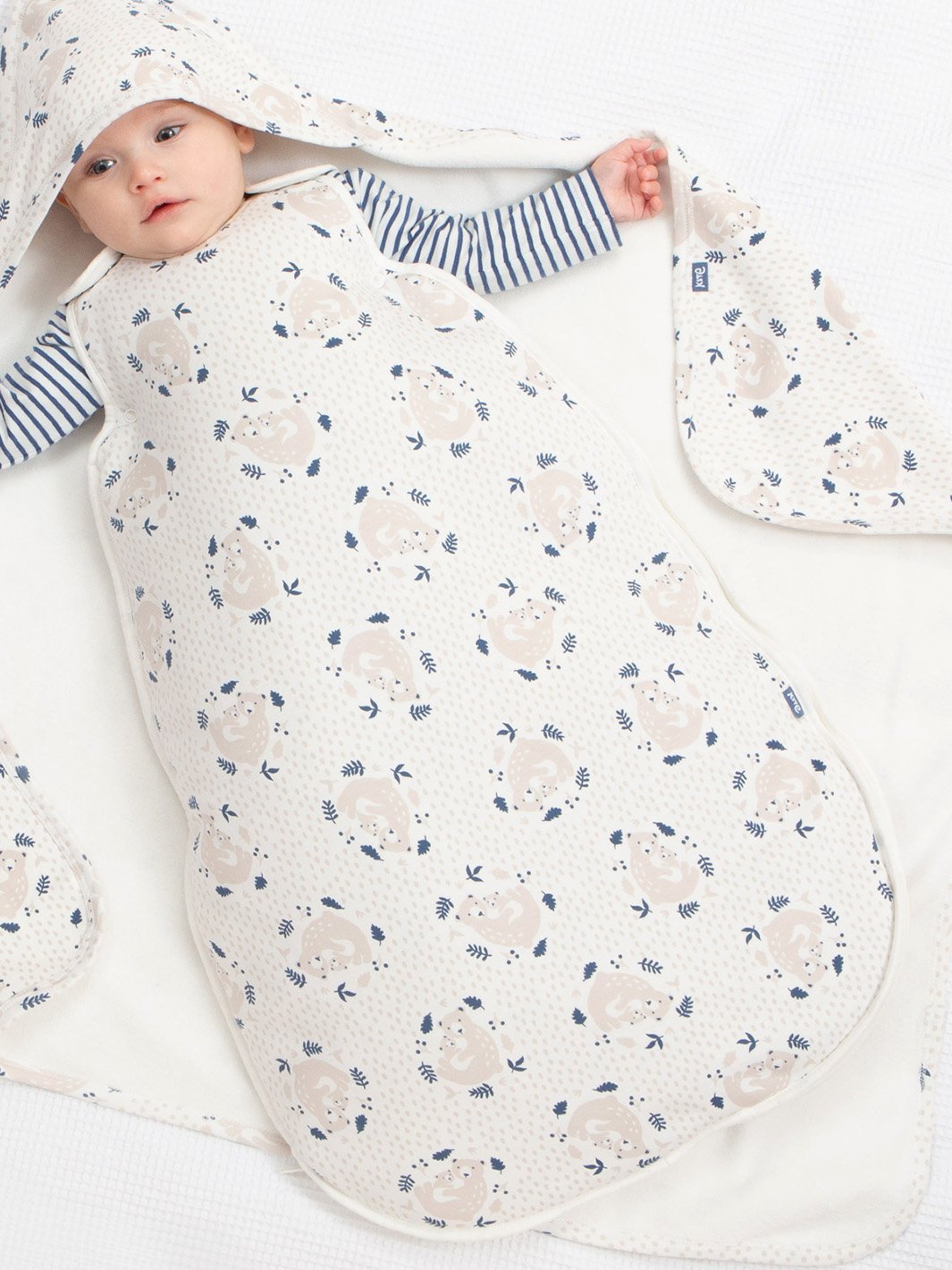 Bebé descansando en saco de dormir crema con estampado de osito abrazable, destacando su suavidad y comodidad.