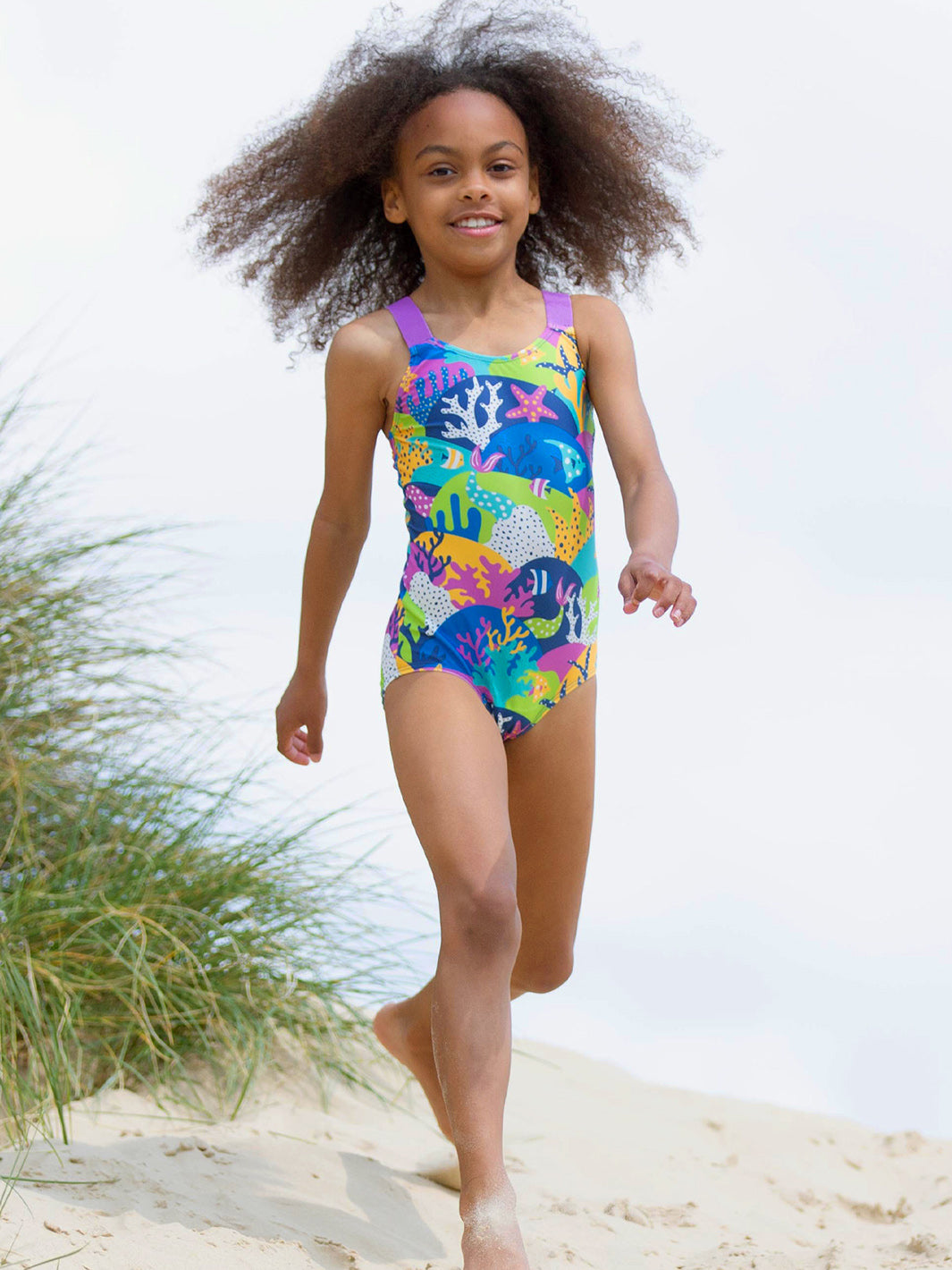 Niña usando el traje de baño arrecifes con protección UPF 50+ en la playa, diseño seguro y ecológico.