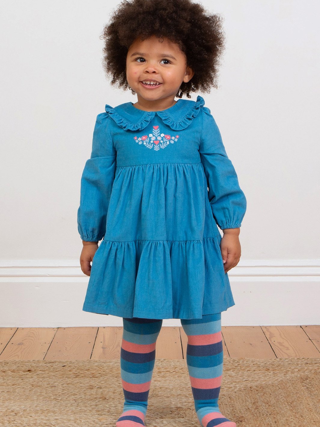 Niña usando el vestido azul francés de manga larga, destacando la falda con volantes y el bordado floral en el pecho.