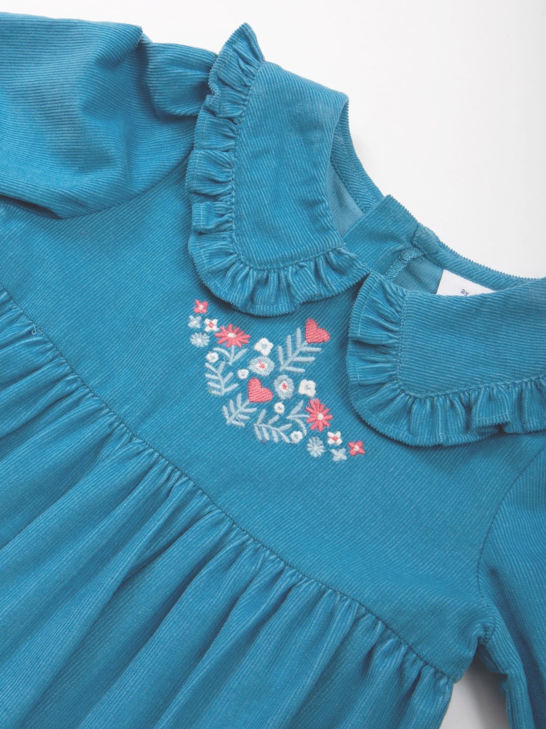Primer plano del cuello de muñeca con volante y bordado de flores en el vestido de cotelé azul francés, resaltando la textura y el diseño.