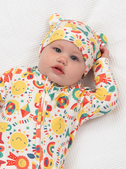 Bebé usando gorrito con orejitas, estampado de soles y arcoíris en colores vivos, de algodón orgánico.