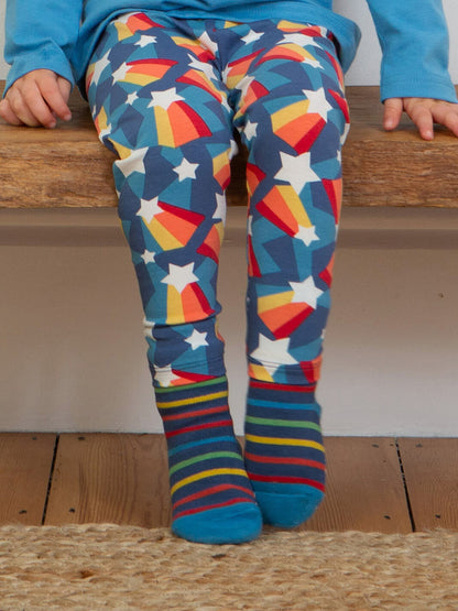 Niño sentado usando leggings de estrellas con calcetines de rayas azules y rojas antideslizantes de algodón orgánico.