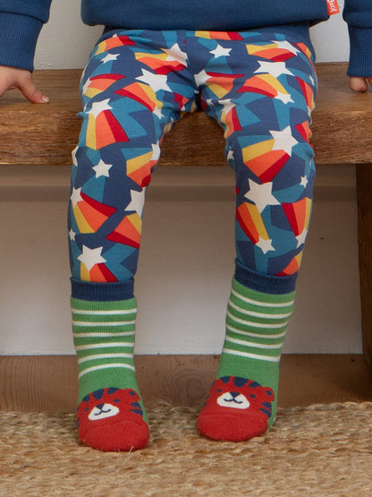 Niño sentado usando leggings de estrellas con calcetines verdes con cara de tigre rojo antideslizantes de algodón orgánico.
