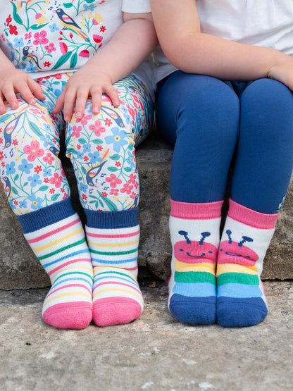 Niñas usando calcetines antideslizantes oruga rosa de algodón orgánico, con rayas multicolor, ideales para primeros pasos.